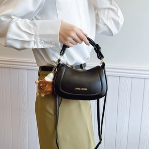 Minimalist black crescent crossbody bag with gold hardware and plush bear charm