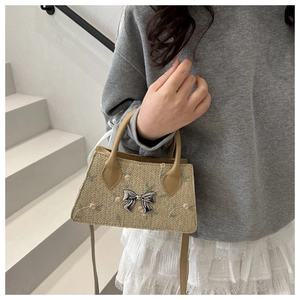 Detail of woven straw handbag featuring floral embroidery and silver metal bow accessory