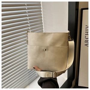 Detail of cream bucket bag with wide strap and gold metal decor on front pocket