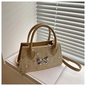 Macro detail of beige woven handbag with pink floral embroidery and metallic bow charm