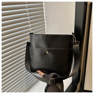 Detail of black PU leather bucket bag with front pocket and gold metal buckle hardware