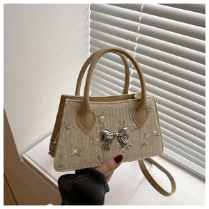 Detail of beige straw bag featuring floral embroidery and a silver metal bow buckle