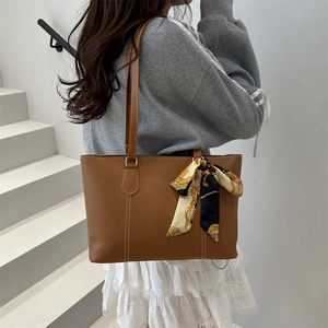 Brown faux leather tote bag with decorative scarf on a model in a minimalist setting