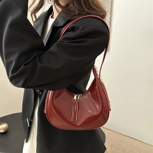 Chic burgundy crescent hobo bag in glossy leather worn by a model in a black blazer