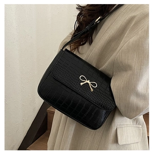 Detail of black crocodile texture shoulder bag with gold bow clasp on beige suit outfit