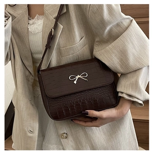 Close-up of a dark brown crocodile texture crossbody bag with a golden bow metal clasp