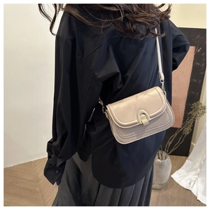 Detail of minimalist beige crossbody bag with gold horseshoe buckle worn by a model
