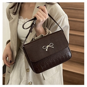 Detail of dark brown crocodile texture bag with gold bow clasp on a beige outfit