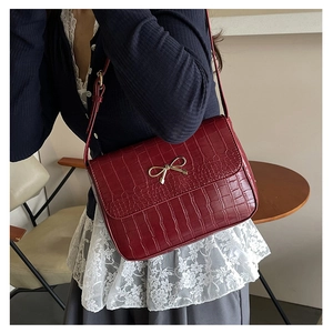 Detail of red croc-embossed shoulder bag with golden bow buckle shown on a model