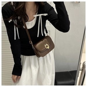 Close-up of brown faux leather crossbody bag with golden horseshoe metal buckle on model