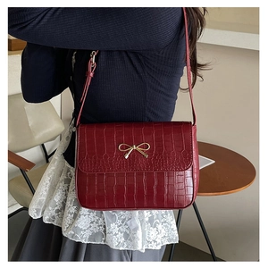 Close-up of wine red crocodile texture bag featuring a golden bow buckle on model