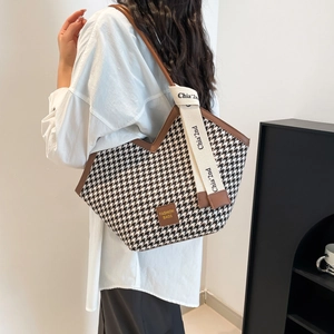 Fashionable houndstooth tote bag with brown leather straps shown on a model's shoulder