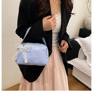Detail of light blue square handbag featuring lace bow and pearl charm on a model