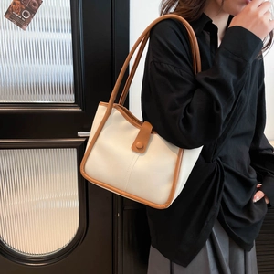 Minimalist white tote bag with brown leather trim and shoulder straps on a black shirt
