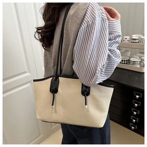 Detail of woven tote bag with contrast black straps and decorative knot feature