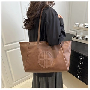 Detailed view of caramel brown tote bag with embossed round logo and leather texture