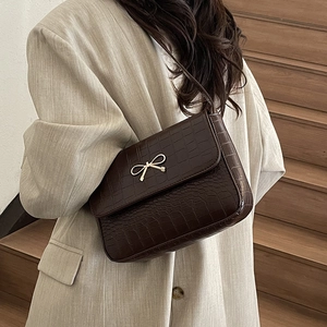 Elegant dark brown crocodile embossed shoulder bag with gold bow clasp on a model