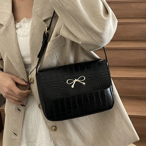 Elegant black crocodile pattern crossbody bag with golden bow worn by a model in casual chic