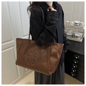 Brown faux leather tote bag with embossed logo worn over the shoulder by a model