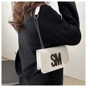 Petit sac blanc avec logo SM et bandoulière en chaîne noire porté avec manteau chic