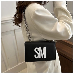 Détail d'un petit sac carré noir chic avec logo SM blanc et bandoulière en chaîne argentée