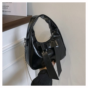 Detail of glossy black hobo bag featuring a decorative bow and silver chain strap