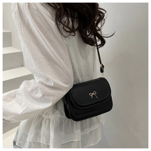 Detail of black crossbody bag featuring a golden bow buckle shown on a model