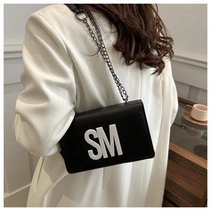 Gros plan d'un sac bandoulière en cuir mat noir avec lettre SM blanche et chaîne
