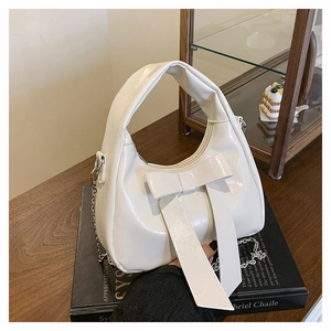 Detailed close-up of white patent leather bucket bag with a large bow and silver chain