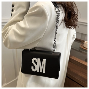 Détail d'un sac à bandoulière noir chic avec logo SM blanc sur un blazer blanc