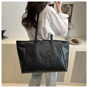 Close-up of a large black tote bag with lychee grain texture and embossed circular logo