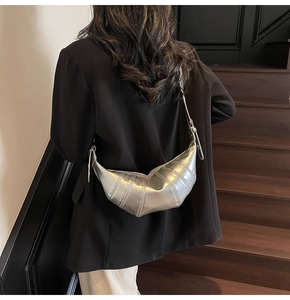 Model wearing a metallic silver croissant bag with distinct stitching over a black blazer