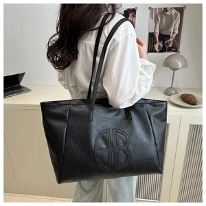 Detailed view of black leather tote bag with unique circular embossed logo on shoulder