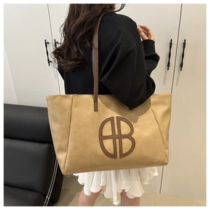 Detail of light brown tote bag featuring circular logo and textured faux leather finish