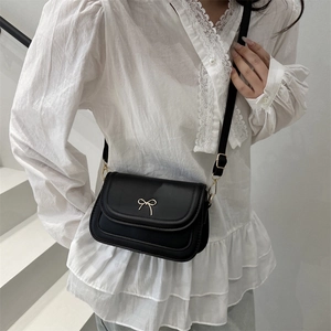 Minimalist black matte leather crossbody bag featuring a golden bow detail and shoulder strap