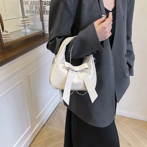 White bucket bag with bow decoration and metal chain shown on model in a modern indoor setting