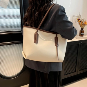 Minimalist beige leather tote bag with brown trim shown on model in modern interior