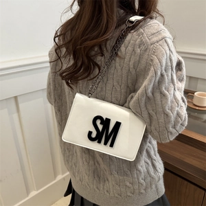 Sac bandoulière blanc chic avec chaîne et logo SM porté sur un pull en maille texturé