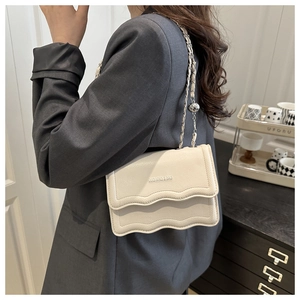 Detail of cream white pebbled leather bag with wave-edge flap and metal chain strap