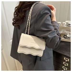 Detail of off-white crossbody bag with wavy pleats and chain strap on a model