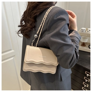 Detail of off-white lychee leather bag with wavy flap and silver metal ball chain strap