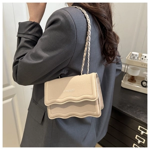 Beige pebble leather crossbody bag with chain strap and wave flap worn by model