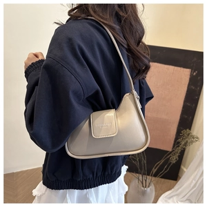Detail view of beige leather shoulder bag with embossed text worn by a model