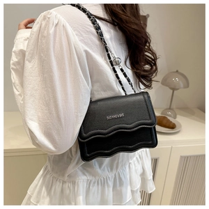 Black pebbled leather crossbody bag with wavy flap edge and chain strap on a model