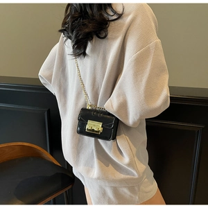 Détail d'un sac carré noir brillant avec bandoulière chaîne dorée sur une tenue grise