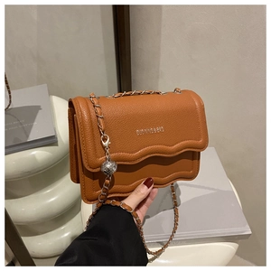 Detail of caramel lychee grain leather crossbody bag with wave edge and silver chain