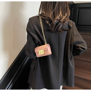 Mini sac rose avec bandoulière chaîne dorée porté sur une veste de tailleur noire
