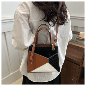 Detail of geometric patchwork handbag with white contrast stitching and crocodile texture
