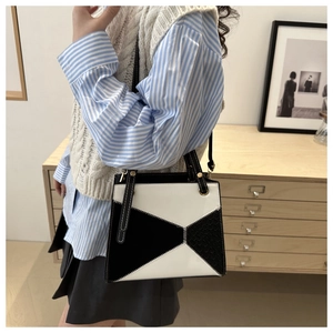 Detail of minimalist geometric black and white handbag with contrast stitching and metal rivets