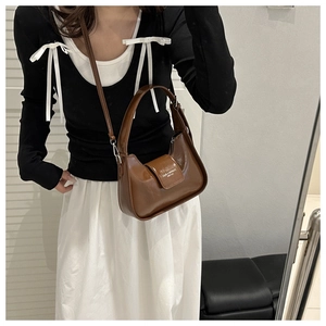 Detailed view of brown glossy leather crescent bag with brand logo and magnetic flap